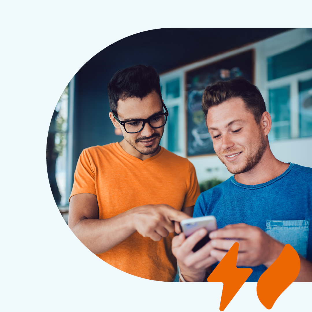 Zwei Personen betrachten gemeinsam ein Smartphone, eine Person zeigt auf den Bildschirm. Unten rechts ein orangefarbenes Strom- & Gas-Symbol.